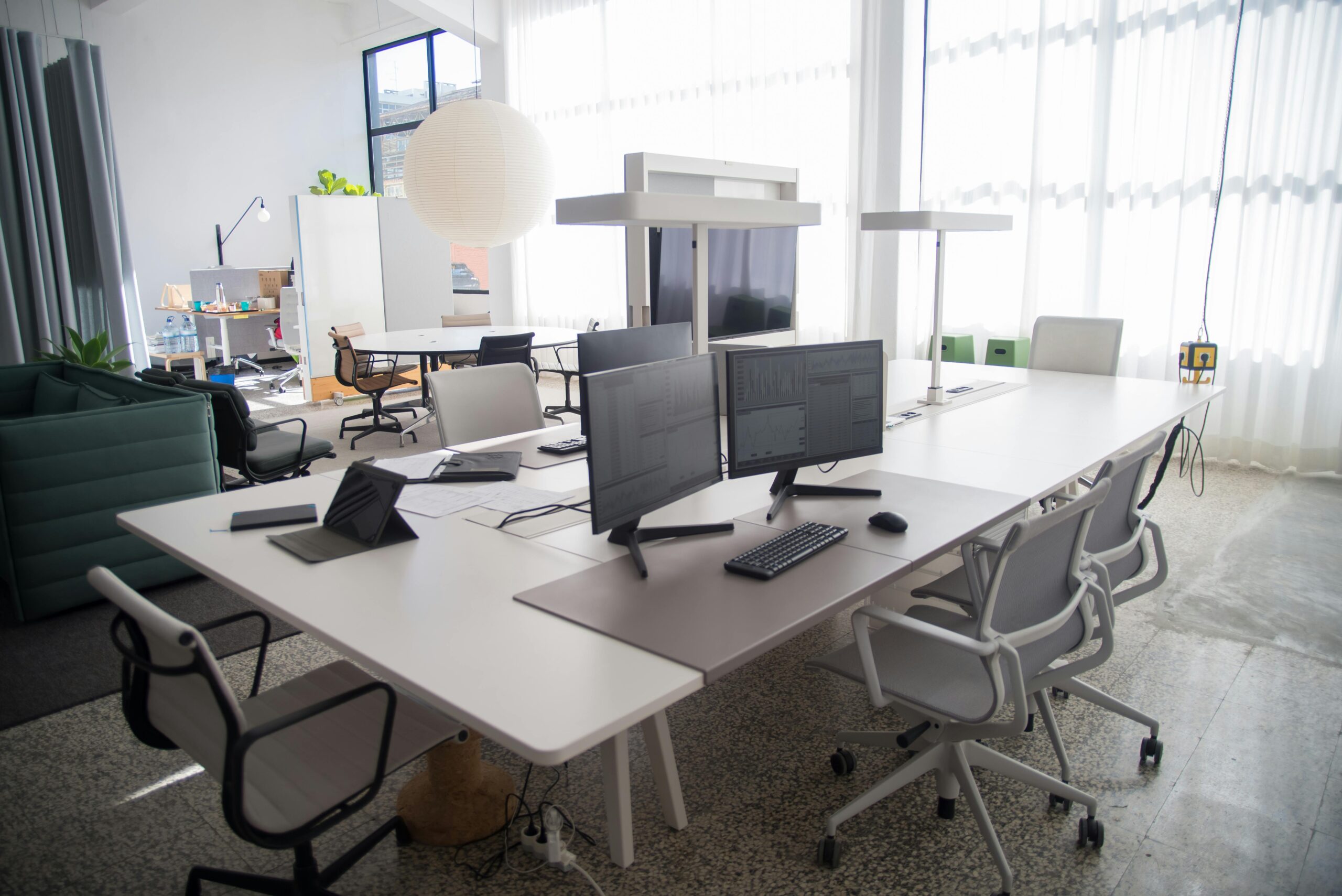 A modern office with multiple workstations and large windows, filling the space with natural light for a bright and productive atmosphere.