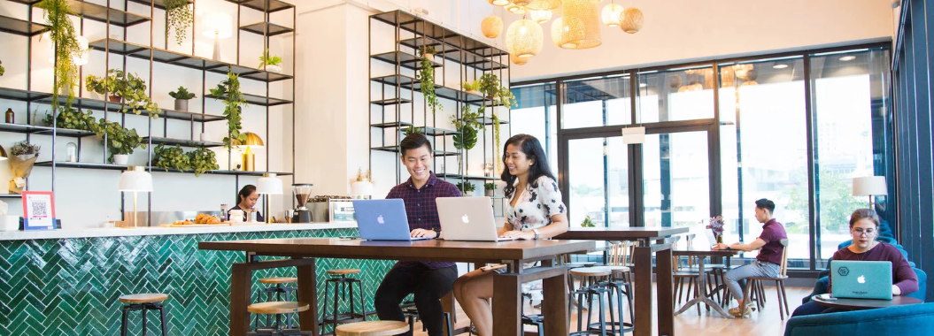 Bright coworking café with hanging lights, green tile bar, modern seating, and people working on laptops