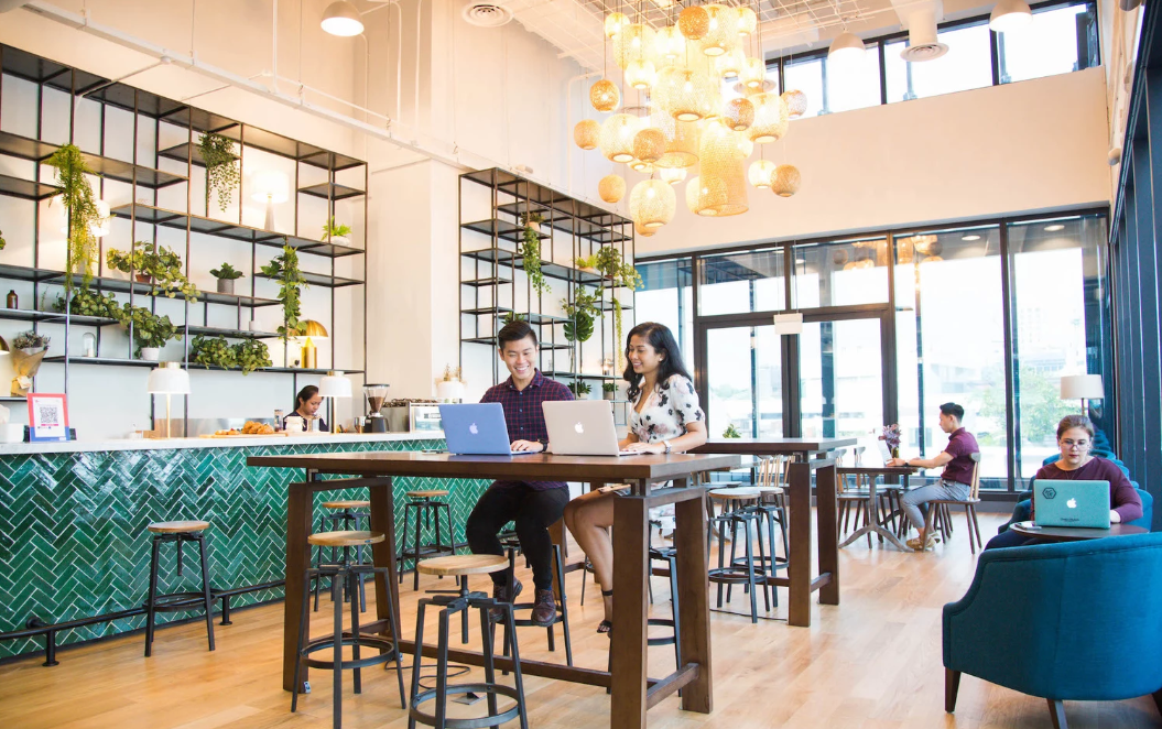 Bright coworking café with hanging lights, green tile bar, modern seating, and people working on laptops