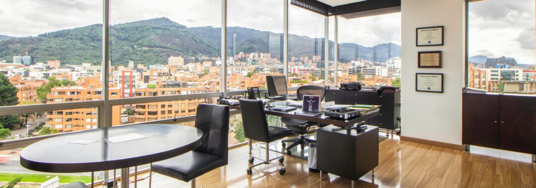 Modern office with floor-to-ceiling windows, city skyline view, wood flooring, and stylish furnishings
