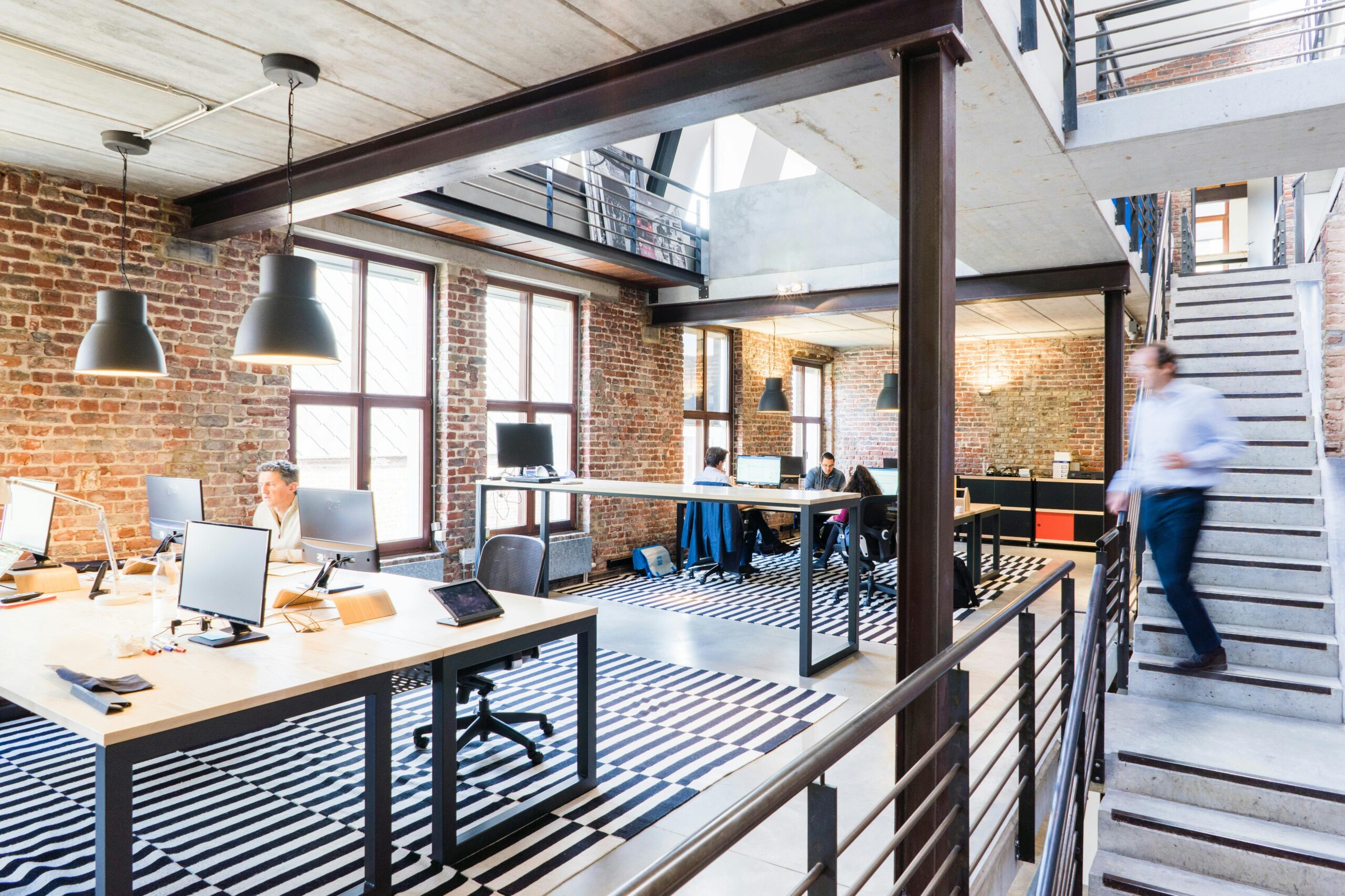 A modern coworking space with brick walls, open desks, and a bright, industrial-style interior.