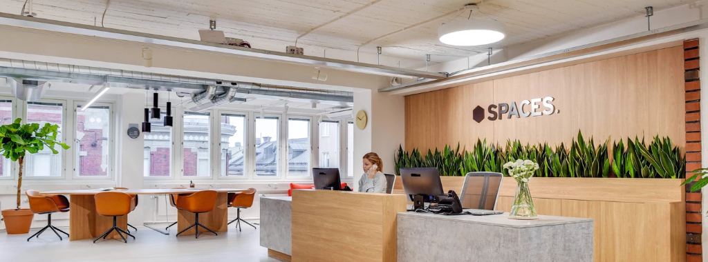 Modern coworking space reception area with bright lighting and plants.