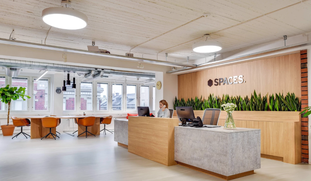 Modern coworking space reception area with bright lighting and plants.