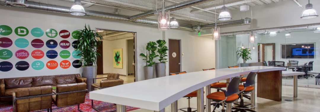 Creative coworking space with lounge area, high table seating, modern lighting, and exposed ceilings