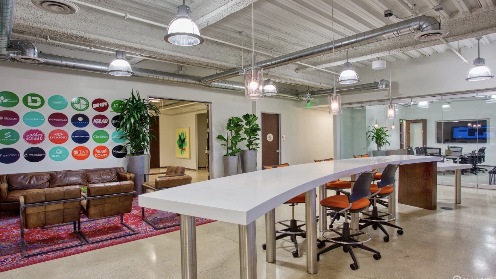 Creative coworking space with lounge area, high table seating, modern lighting, and exposed ceilings